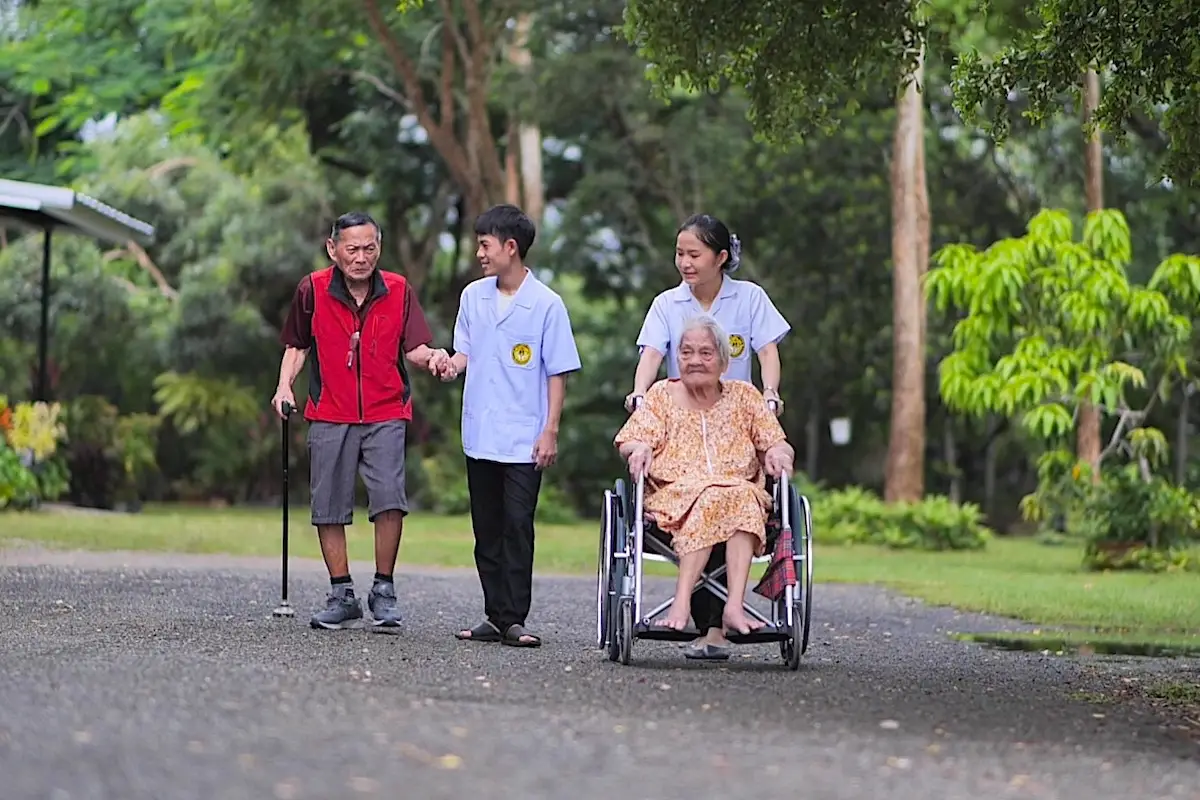 Care staff assisting elderly residents with walking and wheelchair mobility outdoors